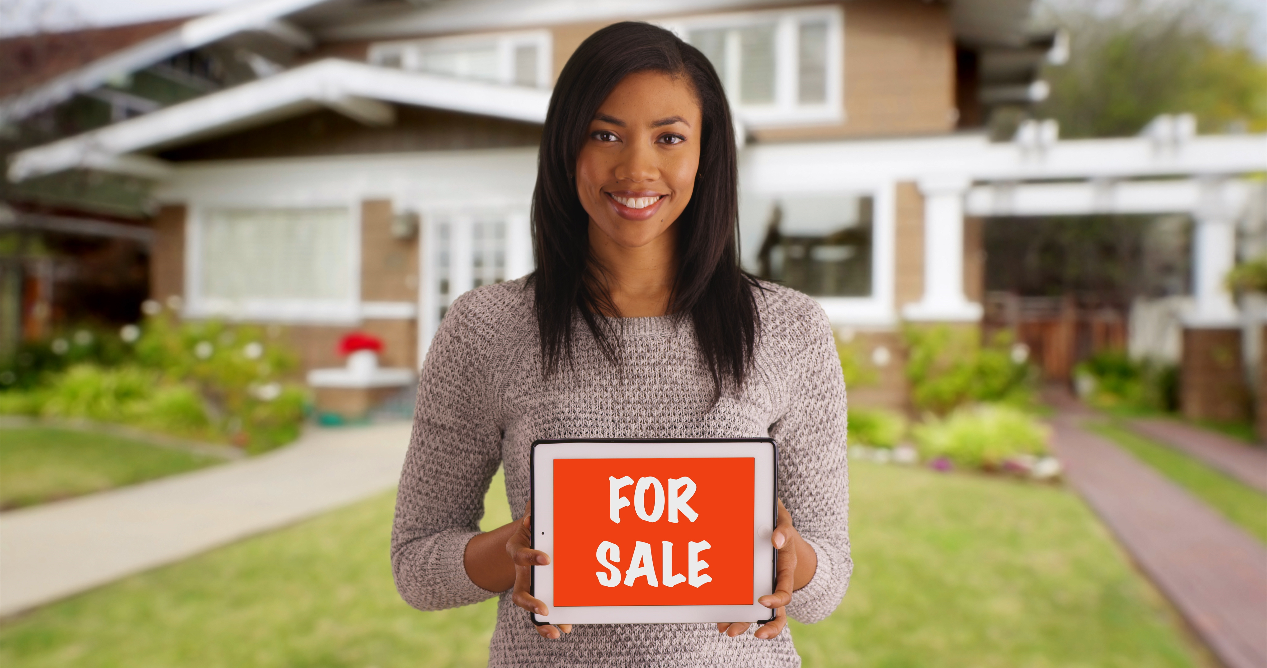 A Black woman holding a FOR SALE sign.