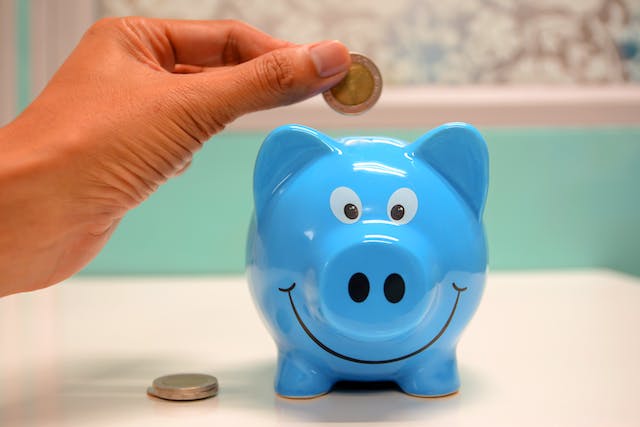 A person putting coins in a blue piggy bank.