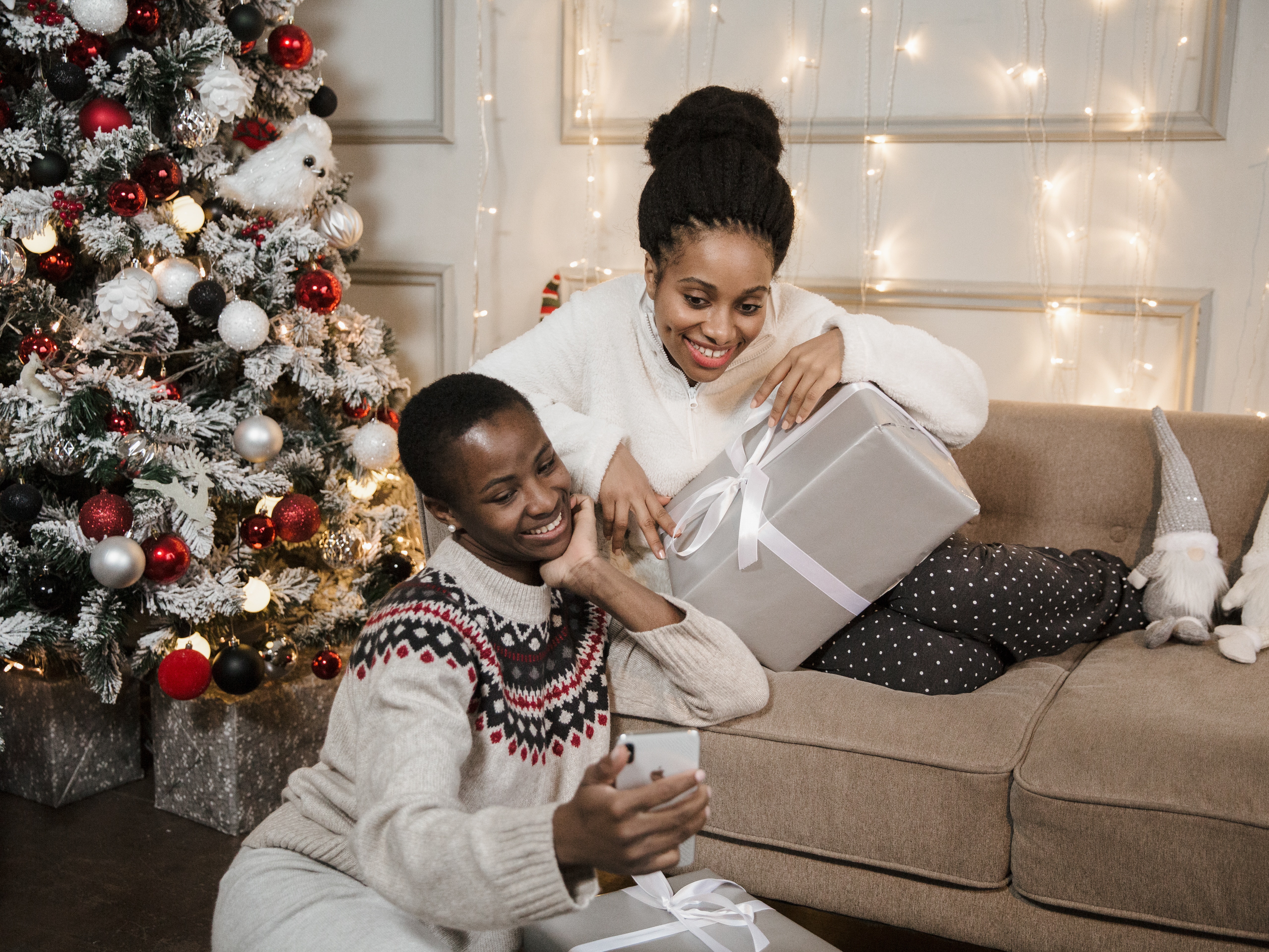 Two women sitting beside a Christmas tree on video chat.