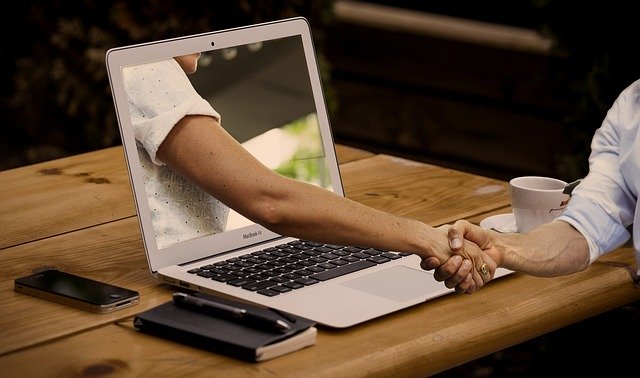 Person from the laptop screen shaking hand with real human sitting by the desk to illustrate building a strong social media presence