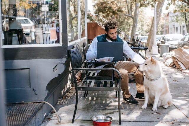 A man sitting at an outdoor café with his laptop, petting a white dog while living in Nashville as an expat