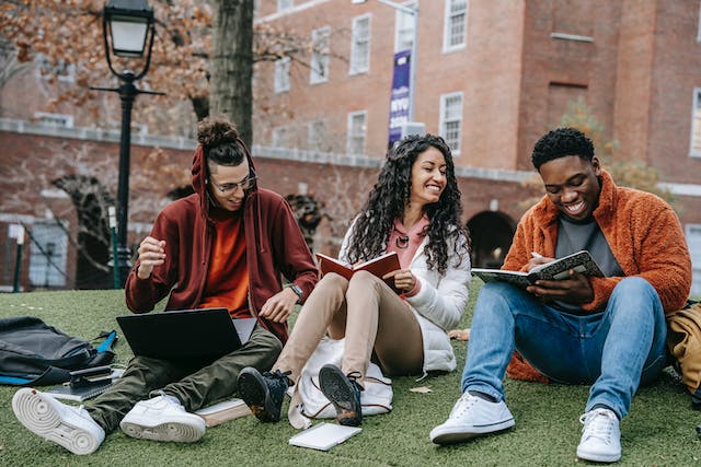Happy students sitting on green grass and studying