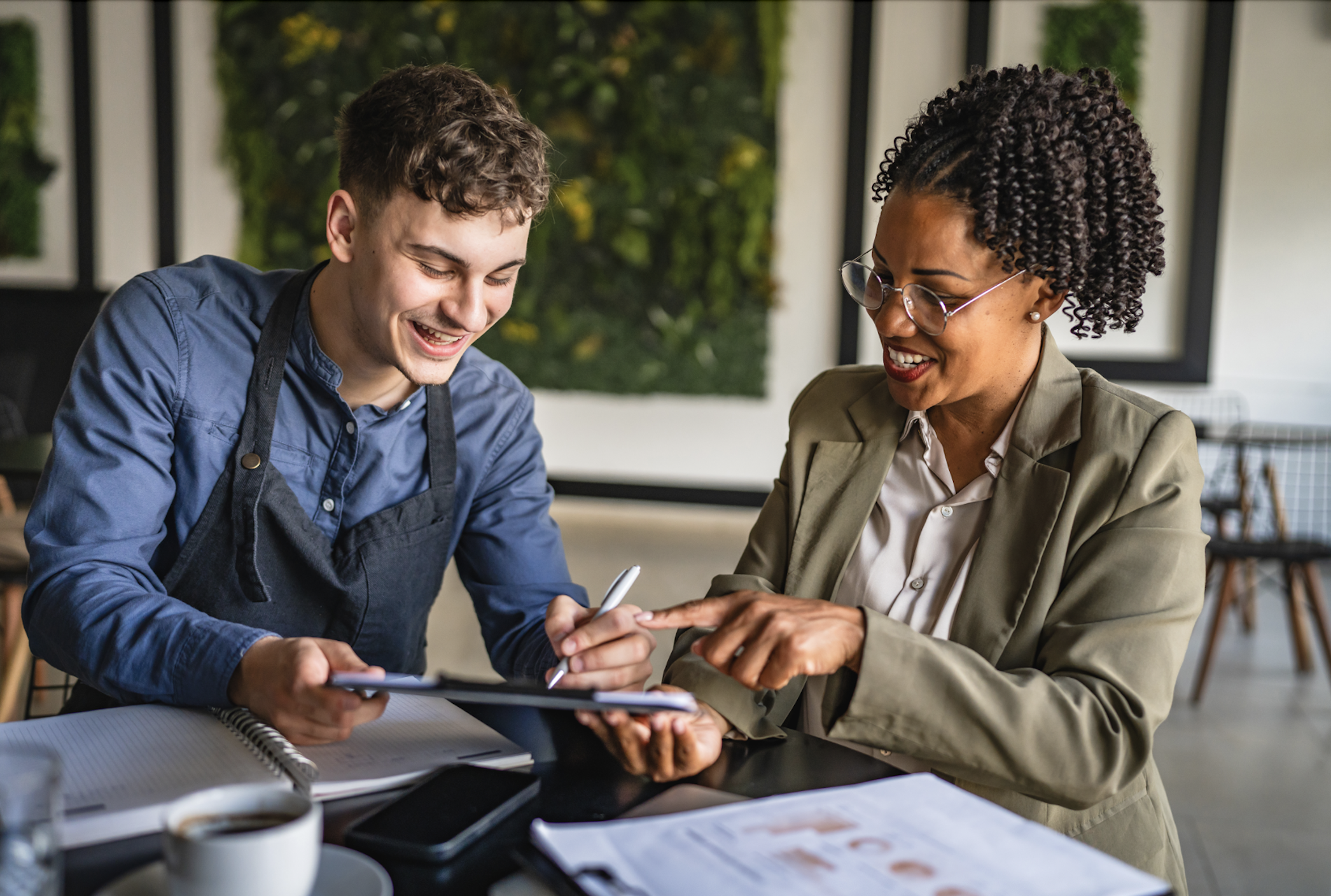 Two small business professionals review financial documents and business data together while discussing cash flow management and financial planning.