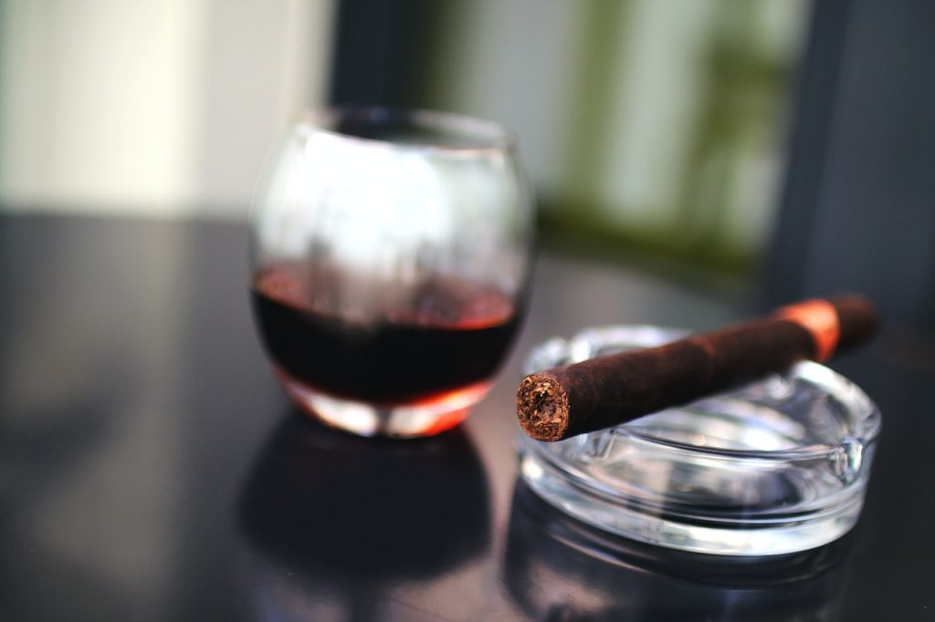A lit cigar in an ashtray and a glass of some drink next to it