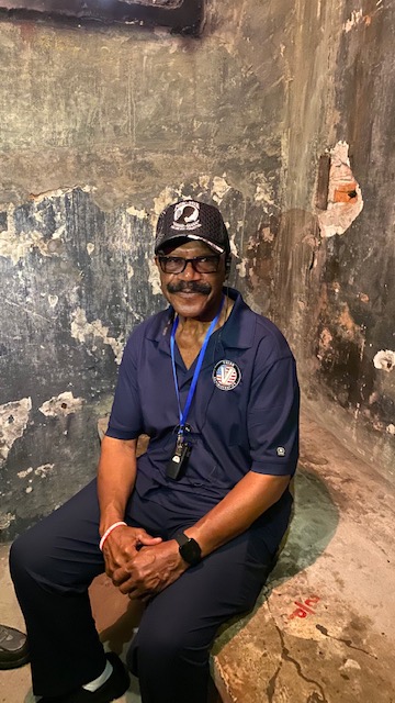 Lt. Col. James Williams sits in cell where he was interrogated and tortured while imprisoned. (Courtesy: Valor Administration)
