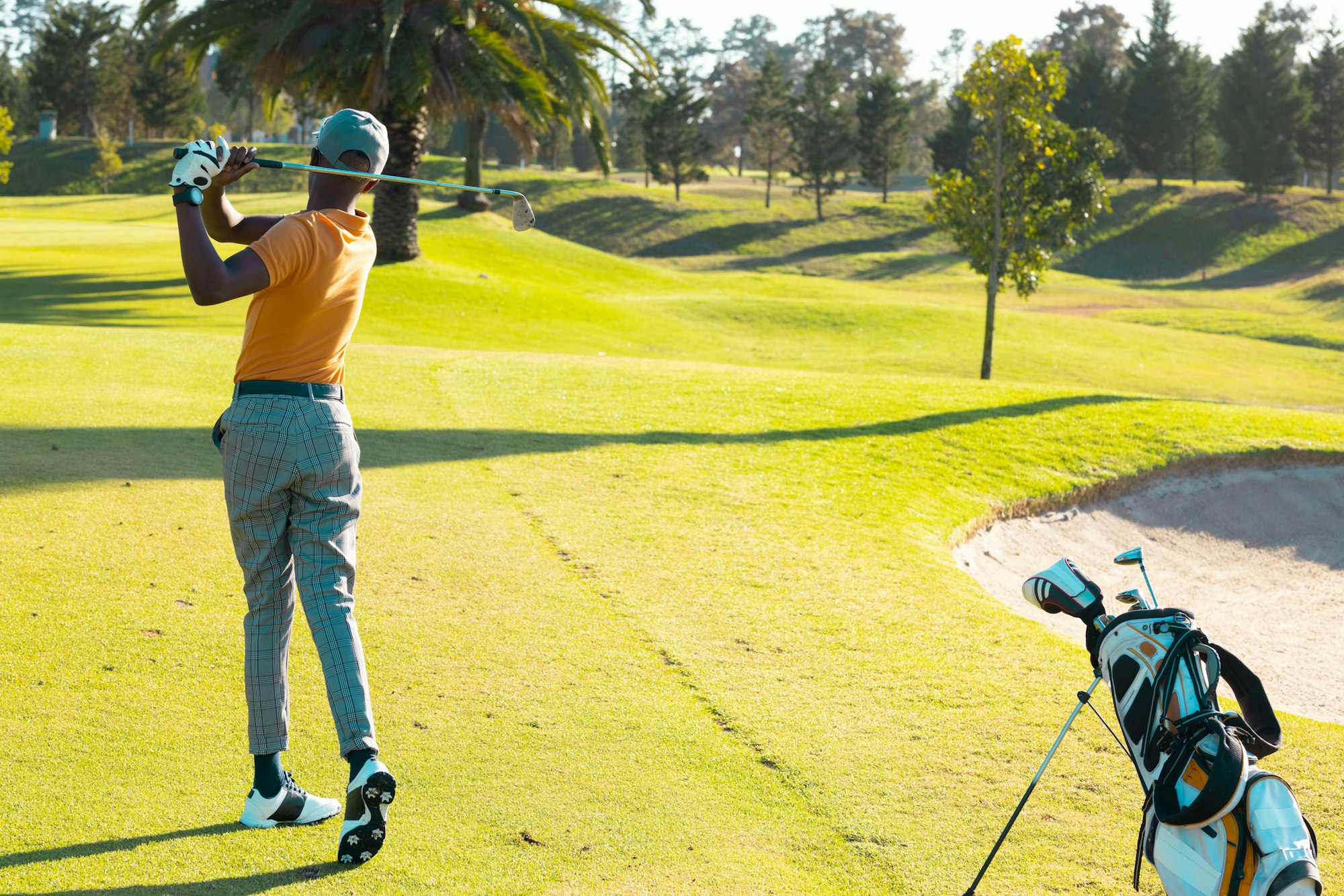 African american young man playing golf with golf club on grassy land at golf course in summer