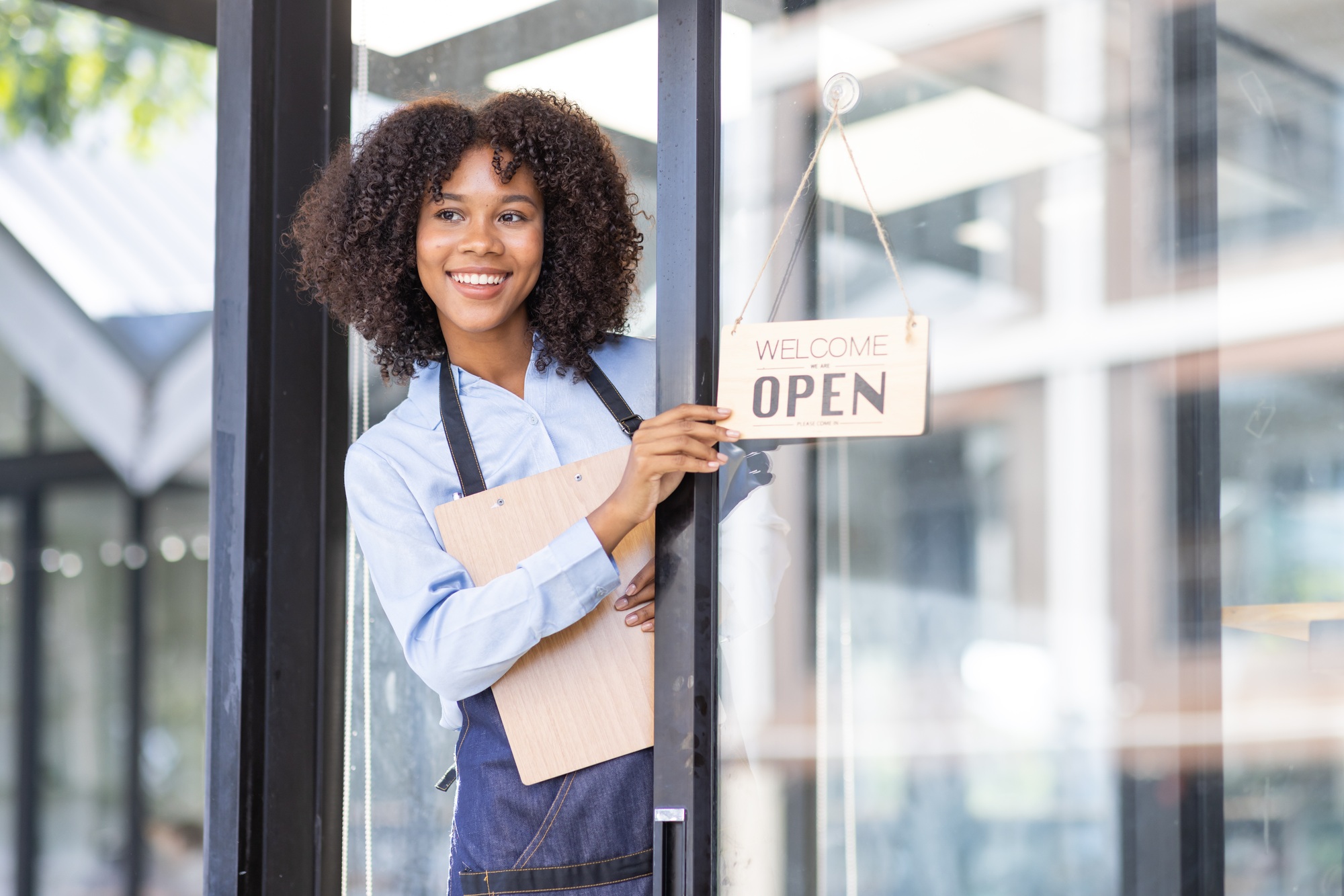 Happy business owner standing at restaurant entrance. Portrait of african american business woman
