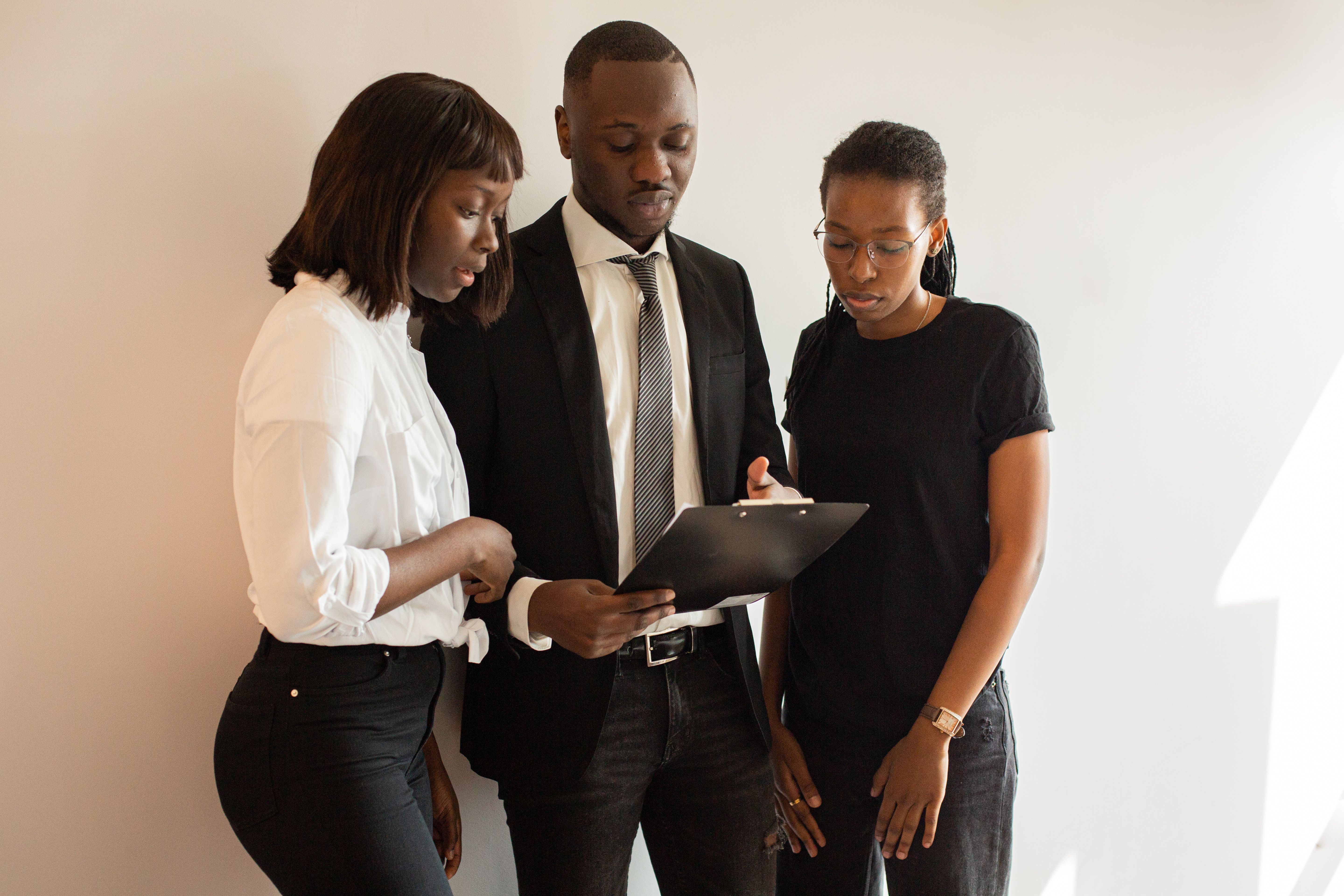 A team of African American professionals discussing work around a clipboard in an office setting.