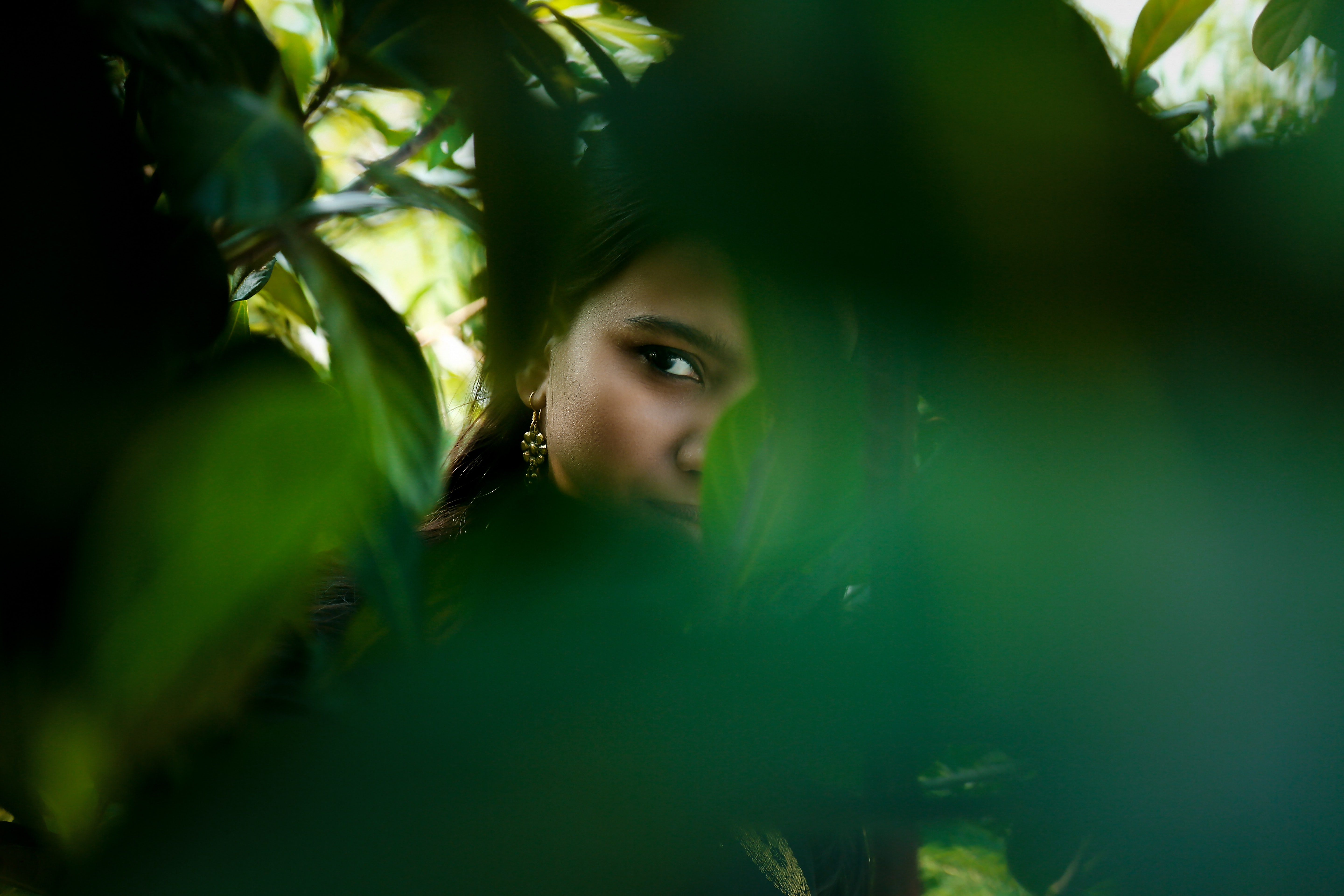A girl hiding behind large green leaves.