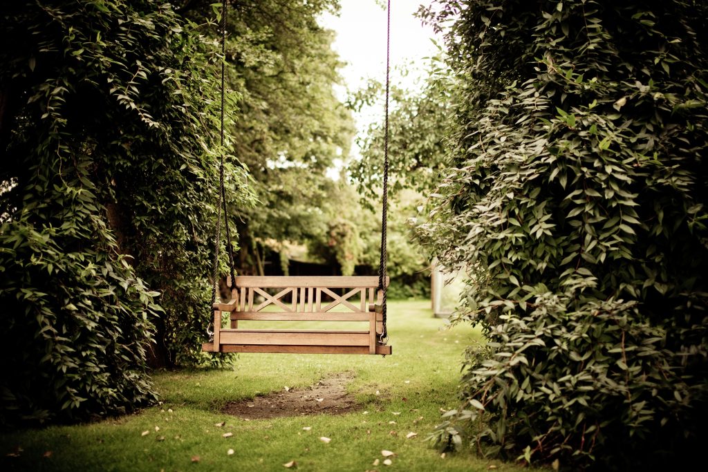 A wooden swing surrounded by trees and plants.