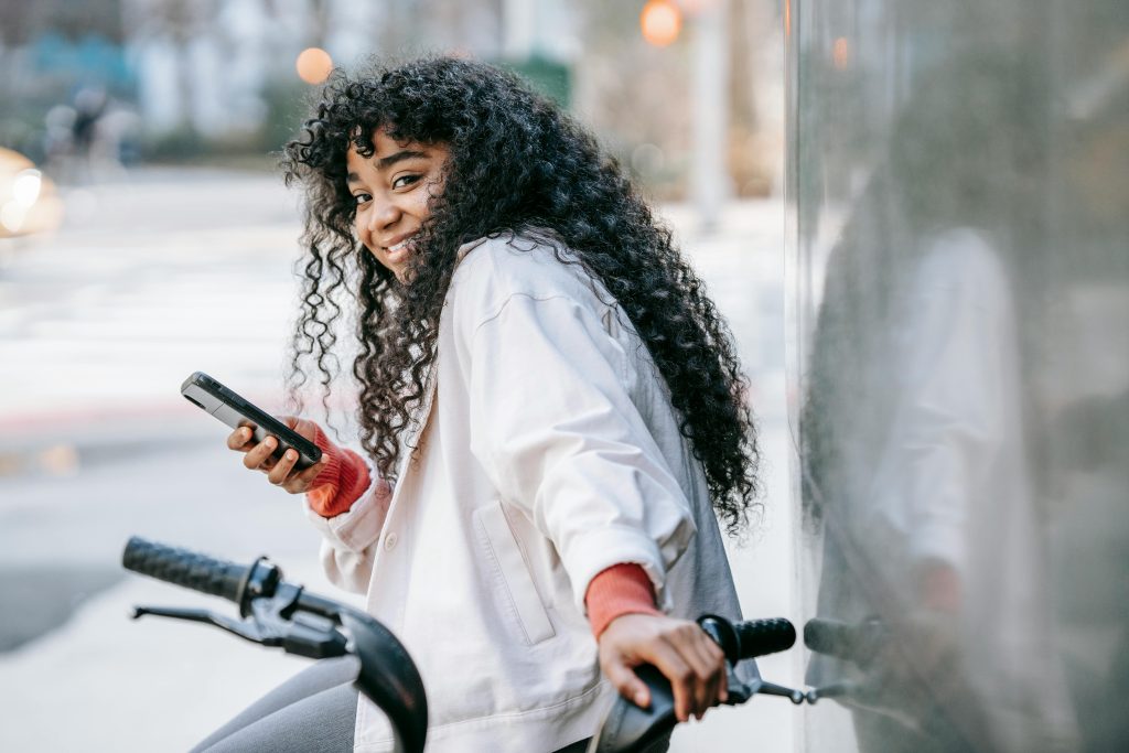 Young woman smiling, holding a phone and a bicycle 