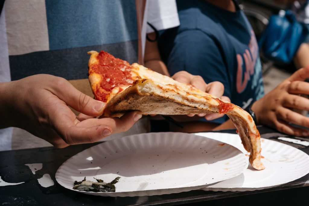 Young male eating traditional italian pizza on paper plate